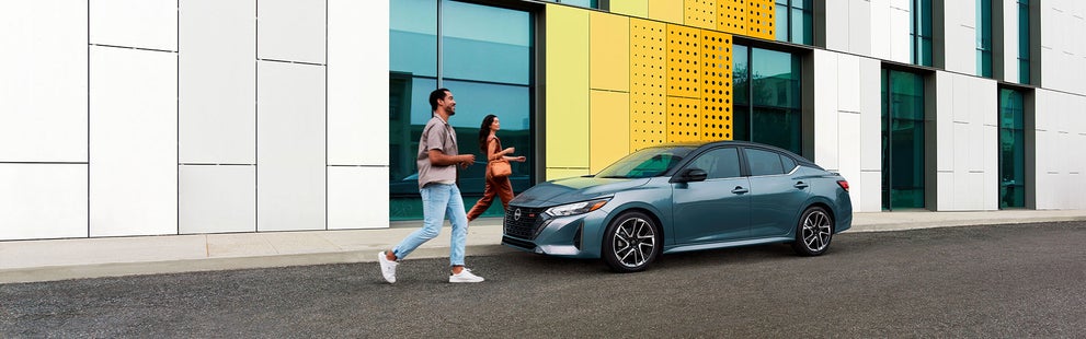 Smiling couple walking towards a parked Nissan Sentra