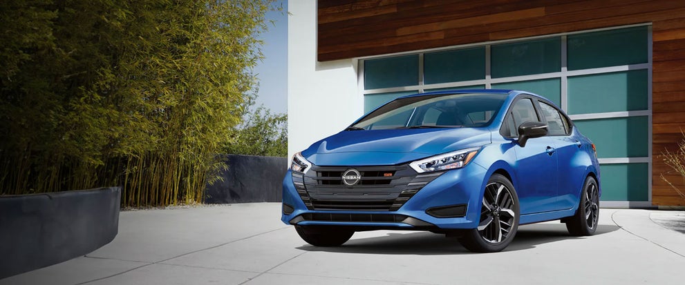 2024 Nissan Versa parked in a driveway in front of a modern garage