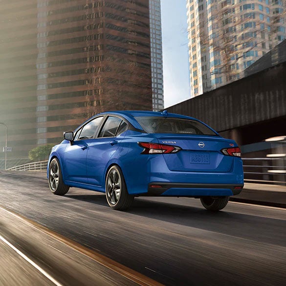 2024 Nissan Versa driving down a city highway with tall skyscrapers in the background