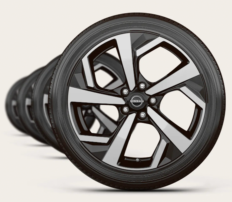 Several black tires with silver and black Nissan rims lined up in a row and receding into the background.